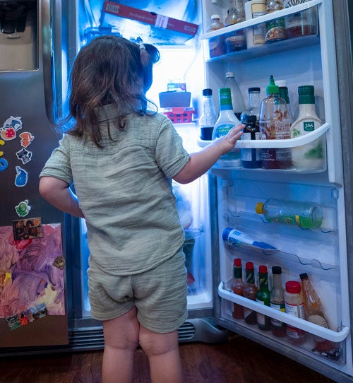 Young girl holding refrigerator door open